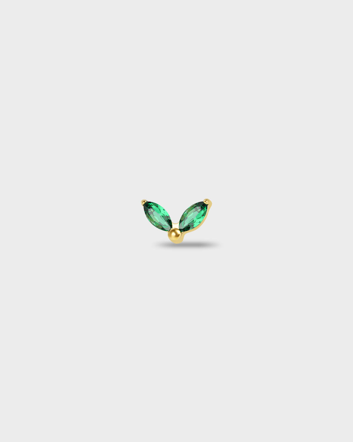 Gold titanium earring with two marquise-cut emerald green stones set in a simple leaf-style arrangement, on a light rgray background.