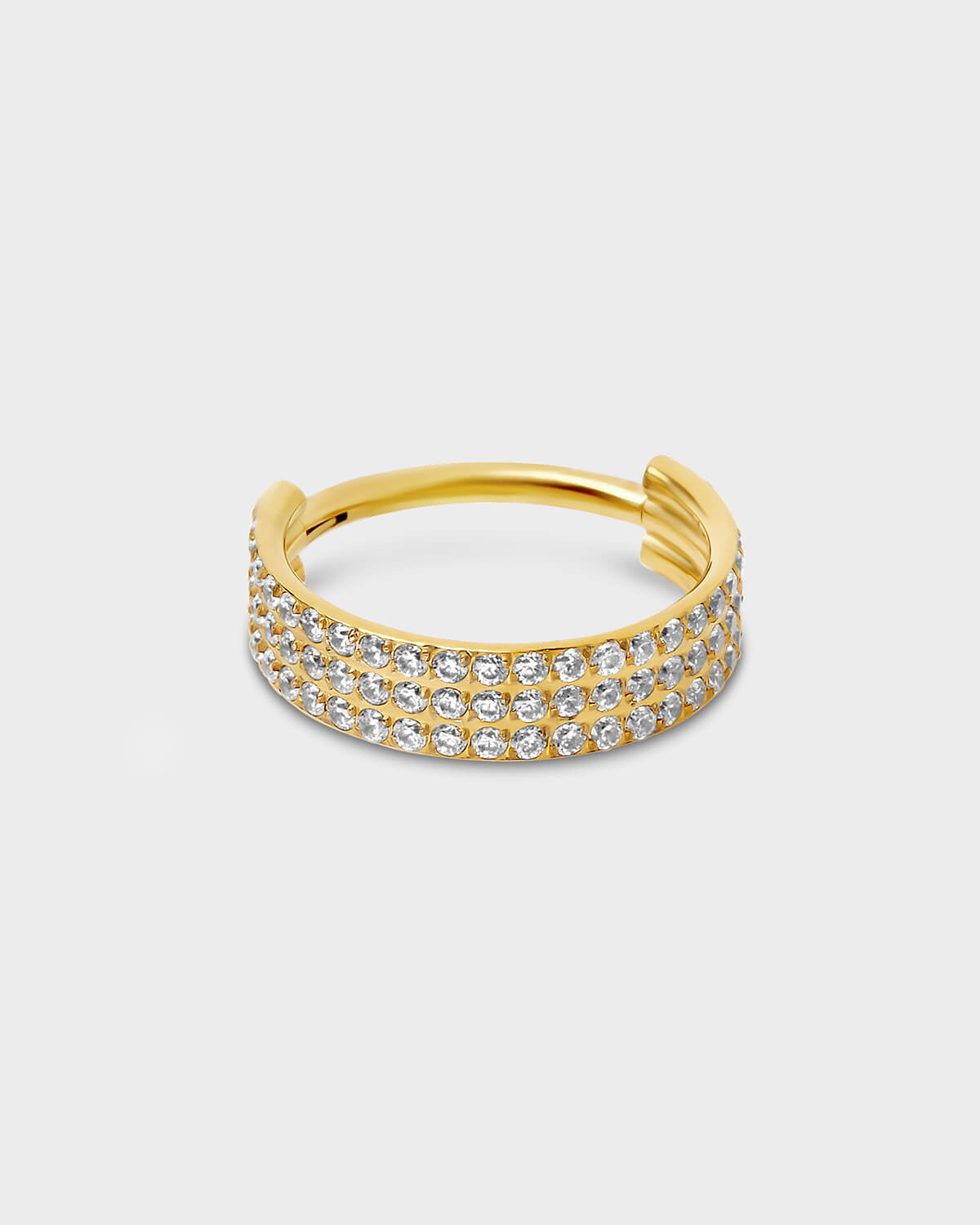 Gold titanium triple and hinged licker ring with pave clear gemstones sat on a light gray background.