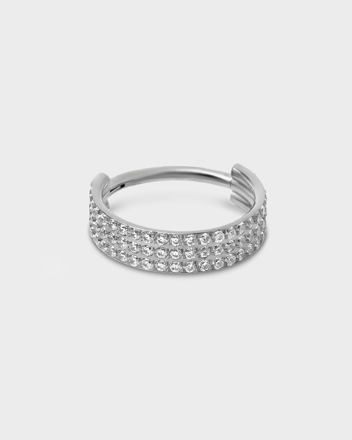 Polished silver titanium triple and hinged licker ring with pave clear gemstones sat on a light gray background.
