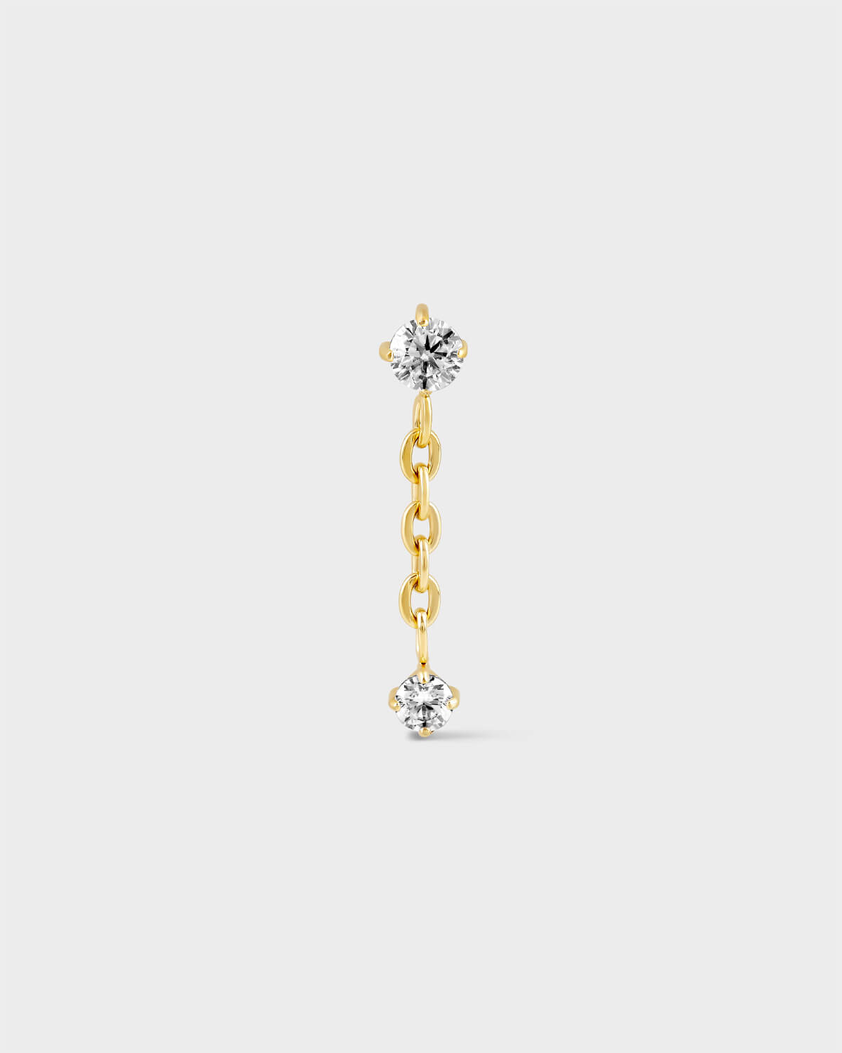 Gold titanium earring with solitaire and chain dropping to another smaller solitaire on a light grey background.