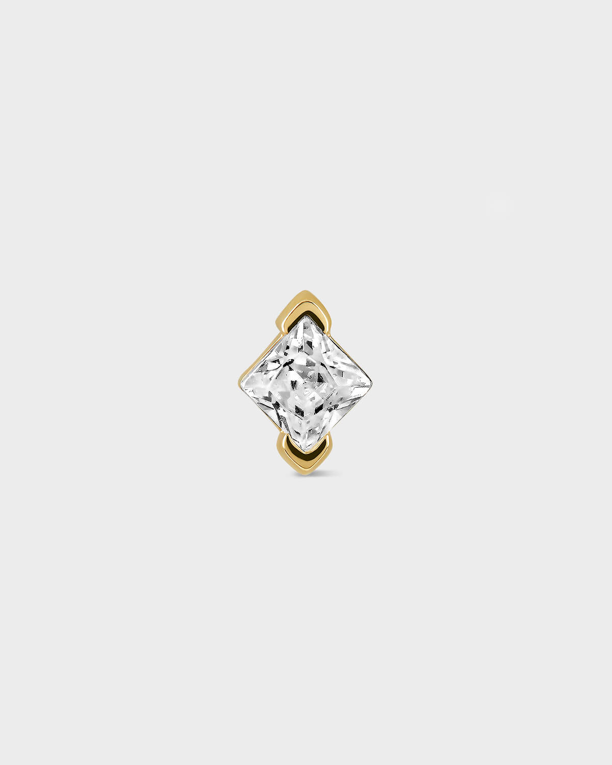 Gold earring with a clear gemstone on a light gray background